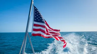 An American flag flies off the stern of a vessel underway.