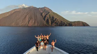 Yacht crewmembers pose on the bow of a yacht in front of an island.
