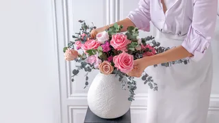 Florist arranging pink flower arrangement in white vase